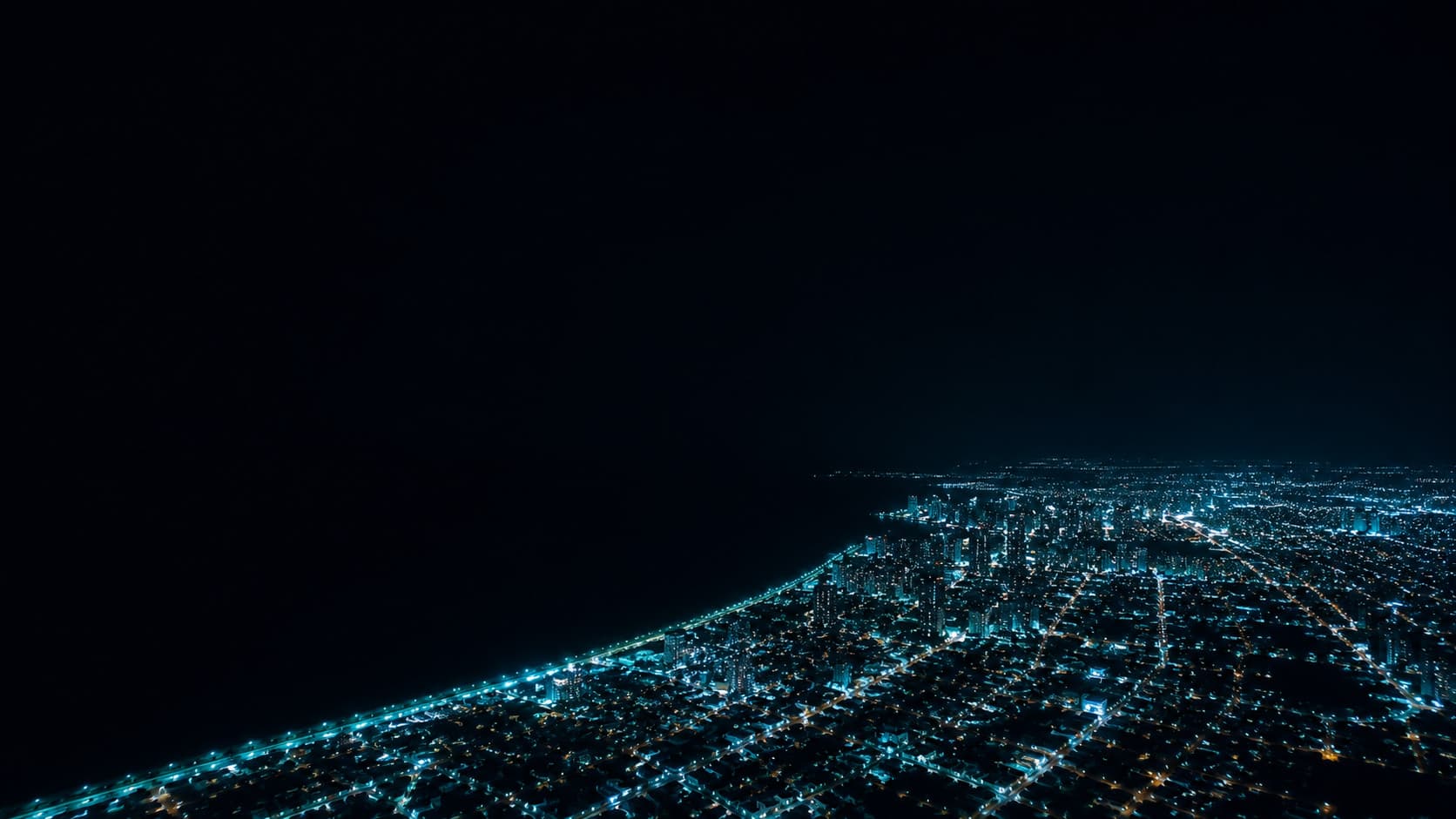 Vista aérea noturna de uma cidade litorânea brasileira, luzes urbanas se estendendo ao longo da costa